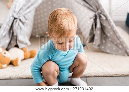 Cute Toddler Boy In Blue Bodysuit Sitting On Hunkers Near Grey Wigwam