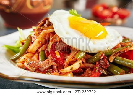 Homemade Kaurma Lagman or Laghman with Vegetables, Beef Meat and Oriental Spices Close Up. Rich Asian Dish of Fried Home-Made Noodles Prepared from a Stringy Dough, Served with Egg