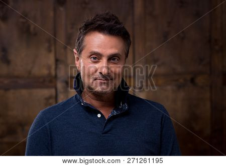 Calm Middle Aged Man In Casual Clothes Standing Against The Brown Wall And Thoughtfully Looking At Y