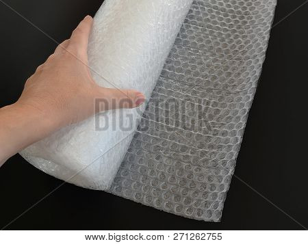 Female Or Woman Hand Holds Transparent Bubble Wrap Roll For Packaging Fragile Items On Black Backgro