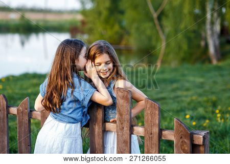Young Girls In White Dresses In The Garden With Apple Trees Blosoming At The Sunset. Two Friends Hug
