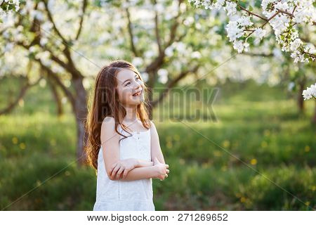 Portrait Of A Beautiful Young Girl With Blue Eyes In White Dress In The Garden With Apple Trees Blos