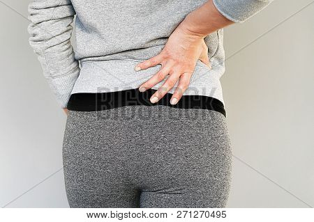 Young Woman With Back Ache Clasping Her Hand To Her Lower Back. Close-up View Of A Young Woman With 