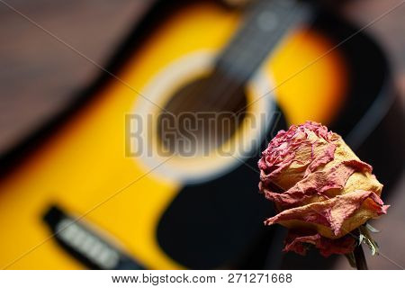 Acoustic Guitar With Dried Roses On The Wooden Table. Template For Advertising A Concert Of Memory O