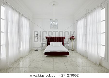 MOSCOW, RUSSIA - DEC 23, 2017: Interior of spacious bedroom with large red bed, chandelier, flowers, windows on both sides in Ligtning Hall of Fotoelite Studio.