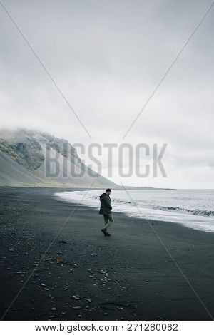 Lonely Man Walks On Grey Black Volcanic Sand Beach