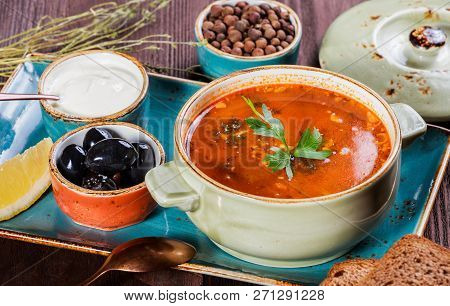 Soup With Meat, Olives, Herbs, Lemon, Sour Cream In Bowl, Black Bread And Spices On Dark Wooden Back