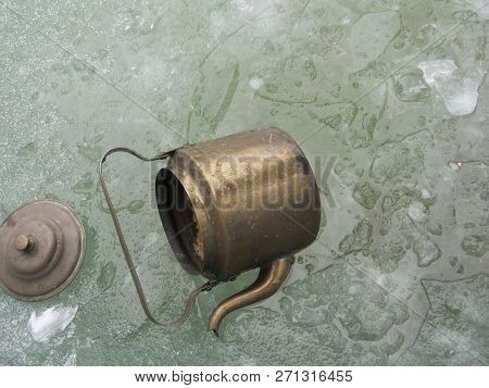 Close-up Of A Retro Bronze Kettle Tipped Over Next To The Ice Hole