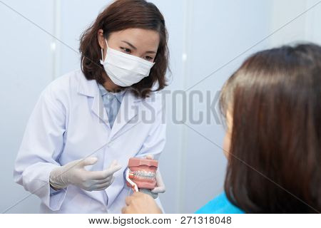 Doctor Explaining Young Atient How To Brush Teeth With Braces