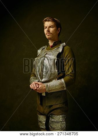 Medieval Knight On Dark Studio Background. Portrait In Low Key Of Brutal Man In Tradishional Retro C
