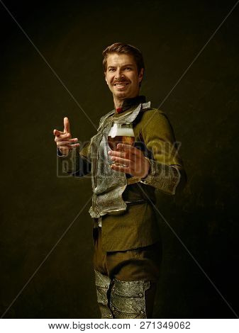 Medieval Smiling Happy Knight With Beer On Dark Studio Background. Portrait In Low Key Of Brutal Man