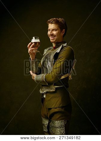 Medieval Smiling Happy Knight With Beer On Dark Studio Background. Portrait In Low Key Of Brutal Man
