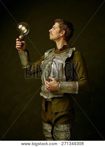 Medieval Knight With Lamp On Dark Studio Background. Portrait In Low Key Of Brutal Man In Tradishion
