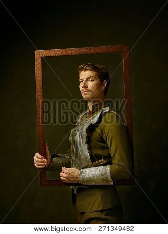 Medieval Knight On Dark Studio Background. Portrait In Low Key Of Brutal Man In Tradishional Retro C