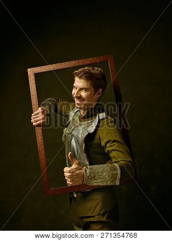 Medieval Knight On Dark Studio Background. Portrait In Low Key Of Brutal Man In Tradishional Retro C