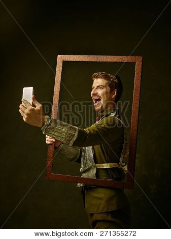 Medieval Knight With Mobile Phone On Dark Studio Background. Portrait In Low Key Of Brutal Man In Tr