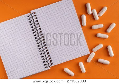 Medicinal Medicine Capsules And Pills Around A Blank Notepad On A Orange Background, Close-up, Top V