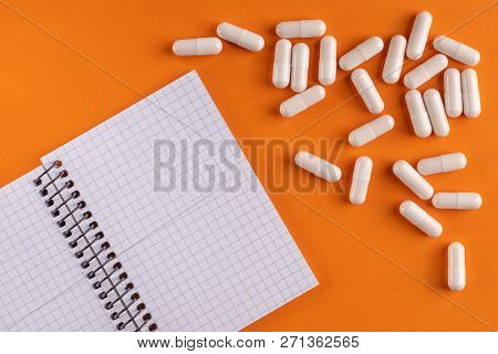 Medicinal Medicine Capsules And Pills Around A Blank Notepad On A Orange Background, Close-up, Top V