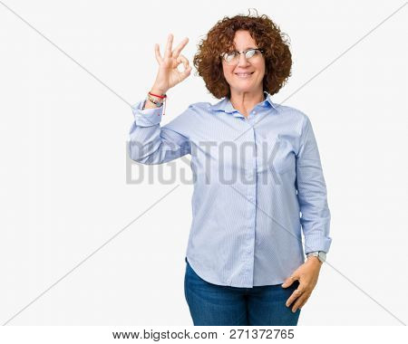 Beautiful middle ager senior businees woman wearing glasses over isolated background smiling positive doing ok sign with hand and fingers. Successful expression.
