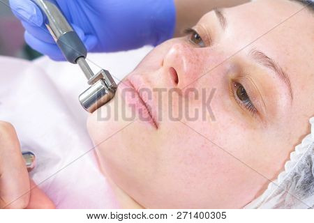 Cosmetologist Makes A Micro-current Procedure For The Face Of A Young Woman. Face Close-up, Side Vie