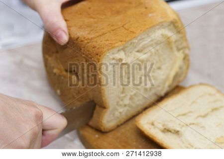 Woman Cutting A Fresh Hot Bread On The Wooden Deskin The Kitchen