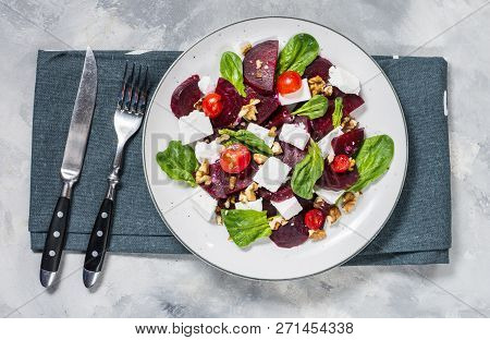Dish With A Salad Of Feta, Beetroot, Cherry Tomatoes And Walnuts On A Concrete Background. Top View