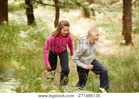 Two children walking together in a forest amongst greenery, three quarter length, side view