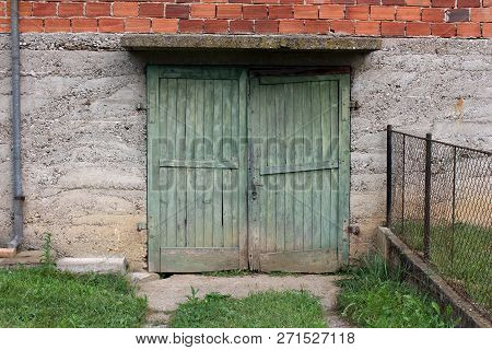 Broken Green Wooden Garage Doors With Rusted Metal Hinges And Small Door Handle Mounted On Concrete 