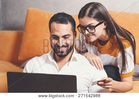 Pretty Long-haired Girl In Pullover Wearing Glasses Holding Credit Card And Sitting On The Yellow So