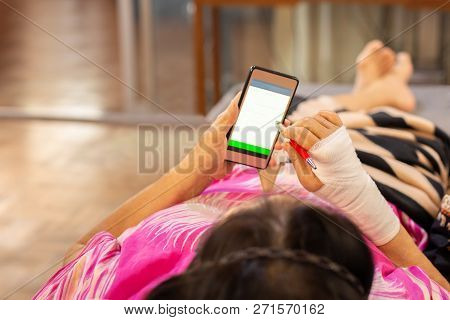 Senior Patient Hand Injured With Bandage Lying Down And Using Cell Phone.