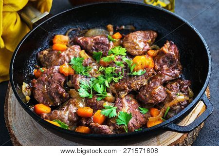 Pork Cheeks Stewed With Vegetables In An Iron Pan, Sliced Bread, Olive Oil, With A Dark Background I