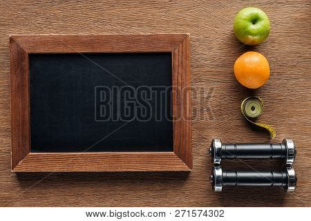 Top View Of Blank Wooden Chalk Board, Fruits, Dumbbells And Measuring Tape, Dieting And Healthy Life