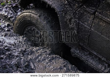 Fragment Of Offroad Car Stuck In Dirt, Close Up. Wheel In Deep Rut Goes Through Mud And Leaves Trail