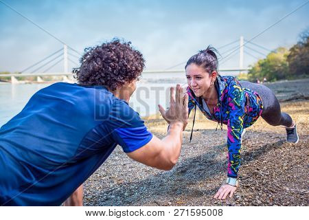 Sporty Couple Giving High Five To Each Other While Doing Push Up Together Outdoors