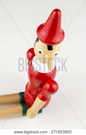 Wooden Pinocchio Doll Sitting Isolated On White Background.