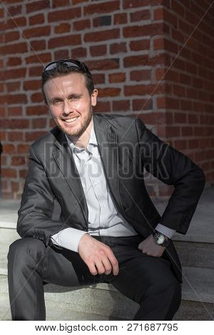 Half Length Portrait Of Young Sniling Man In Suit Sitting On Steps Outside Of His Office Building, P