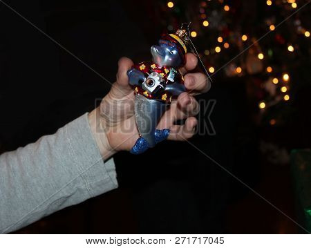 Hand Holds Christmas Tree Ornament Of Dophin With Camera In Front Of Bokeh Christmas Tree