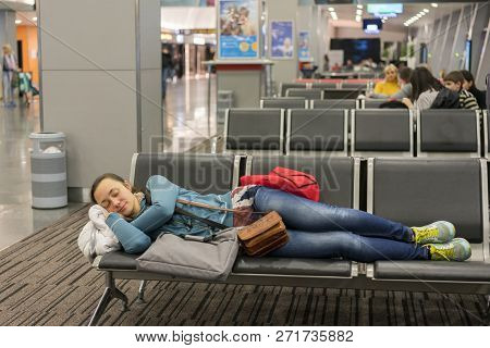Young Woman Sleeping At The Airport While Waiting For Her Flight. Tired Female Traveler Sleeping On 