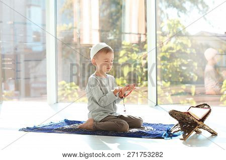 Little Muslim Boy With Misbaha And Koran Praying On Rug Indoors