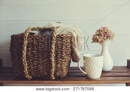 Cozy Winter Interior Details In White And Brown Tones. Basket With Knitted Sweater And Cup Of Coffee