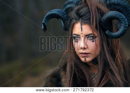 Outdoor Portrait Of Beautiful Scandinavian Viking Woman Warrior With Blue Eyes Wearing Ram Horns. Fe