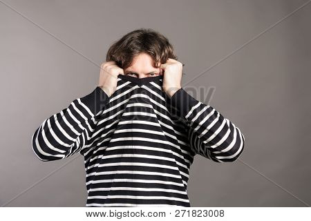 Portrait Of Young Man With Dark Curly Hair Pulling Her Sweater Over Head Having Problems. Male Tryin