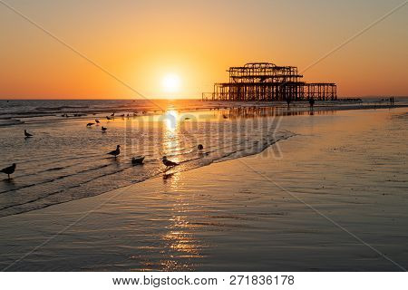 The Old Remains Of Brighton Pier Left Standing In Sea With Beautiful Waves, Seagulls And Local Peopl