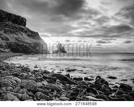 Evening Bay. Sharp Rocks, Black Rounded Boulders, Stony Beach, Sand And Dark Sky.