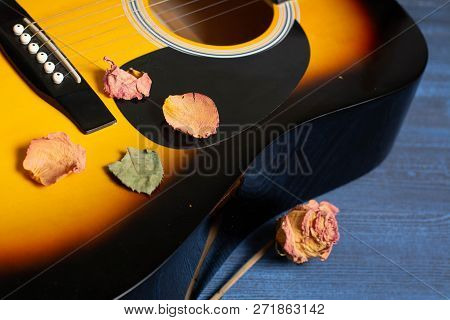 Acoustic Guitar With Dried Roses On The Wooden Table. Template For Advertising A Concert Of Memory O