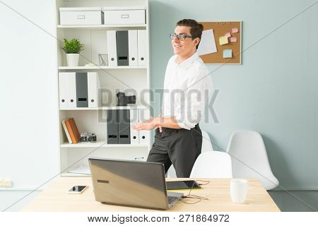 Business, Office, People Concept - Handsome Man In Glasses Stands In The Office Near A Computer And 