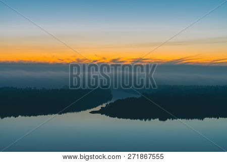 Early Blue Sky Reflected In River Water. Riverbank With Forest Under Predawn Sky. Yellow Stripe In P