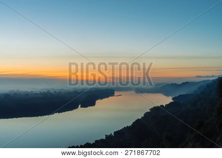 View From High Shore On River. Riverbank With Forest Under Thick Fog. Dawn Reflected In Water. Yello