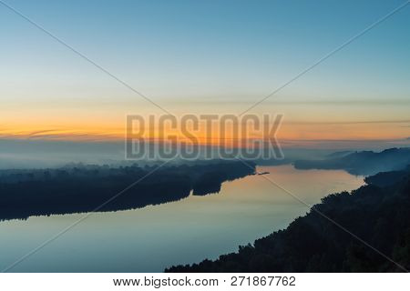 View From High Shore On River. Riverbank With Forest Under Thick Fog. Dawn Reflected In Water. Yello