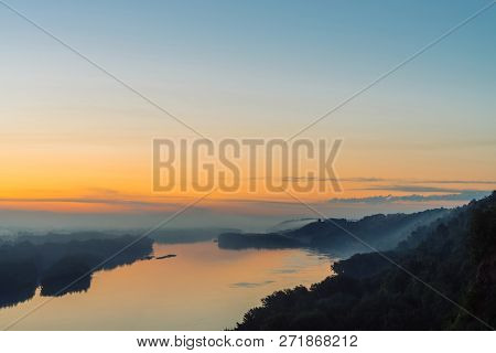 View From High Shore On Broad River. Riverbank With Forest Under Thick Fog. Dawn Reflected In Water.